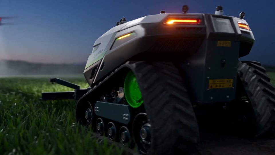 Il drone passa sopra il robot fermo fra le file, al tramonto
