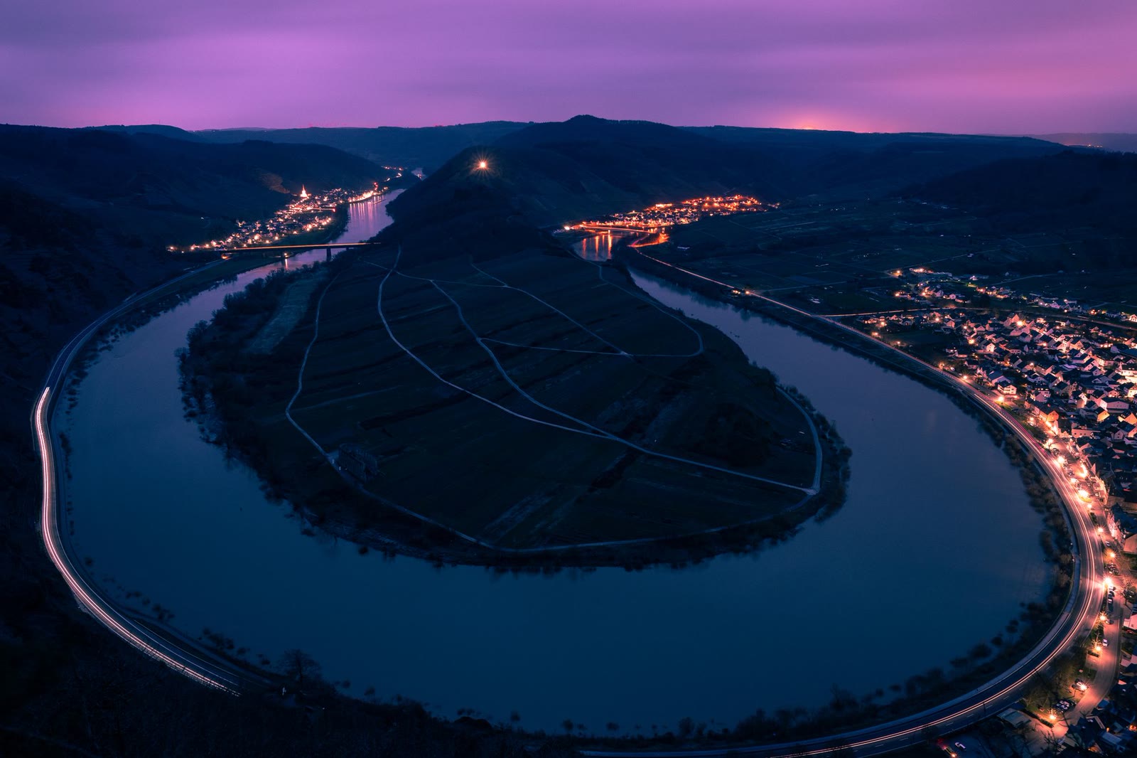 L'ansa di un fiume fra i vigneti, di notte, con le luci del paese